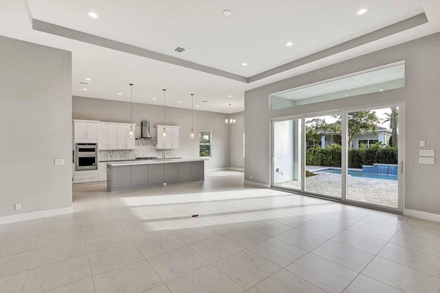 kitchen featuring decorative light fixtures, white cabinetry, a large island with sink, a tray ceiling, and wall chimney exhaust hood