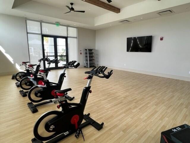 exercise room featuring hardwood / wood-style floors, a tray ceiling, french doors, and ceiling fan