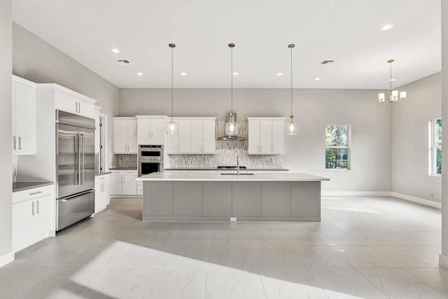 kitchen with wall chimney exhaust hood, a large island with sink, appliances with stainless steel finishes, pendant lighting, and white cabinets