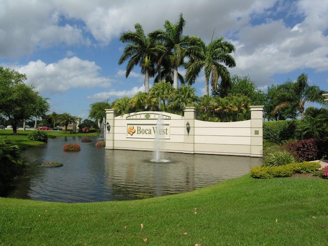 community / neighborhood sign featuring a water view and a lawn