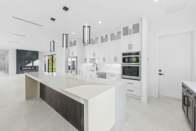 kitchen featuring appliances with stainless steel finishes, decorative light fixtures, sink, white cabinets, and a large island