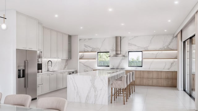 kitchen featuring a large island, white cabinets, wall chimney exhaust hood, and appliances with stainless steel finishes