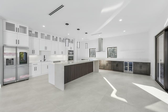 kitchen with pendant lighting, white cabinets, a center island, stainless steel appliances, and wall chimney range hood