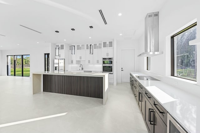 kitchen featuring a spacious island, decorative light fixtures, range hood, and white cabinets