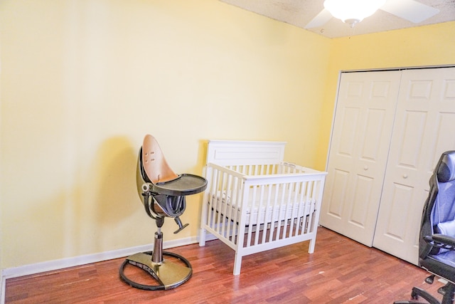 bedroom featuring ceiling fan, wood-type flooring, a crib, and a closet