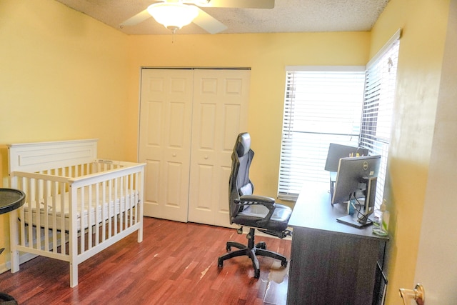 bedroom with a textured ceiling, ceiling fan, a crib, a closet, and hardwood / wood-style flooring