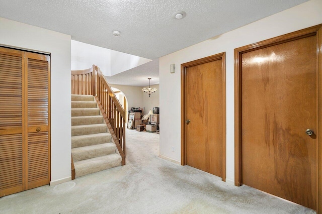 hallway featuring light carpet, a textured ceiling, and an inviting chandelier