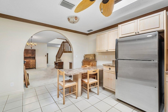 kitchen featuring light tile patterned floors, stainless steel refrigerator, ceiling fan, ornamental molding, and light stone countertops