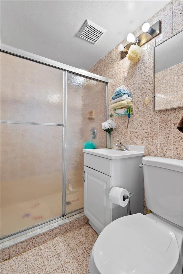 bathroom with vanity, toilet, a shower with shower door, and tile walls