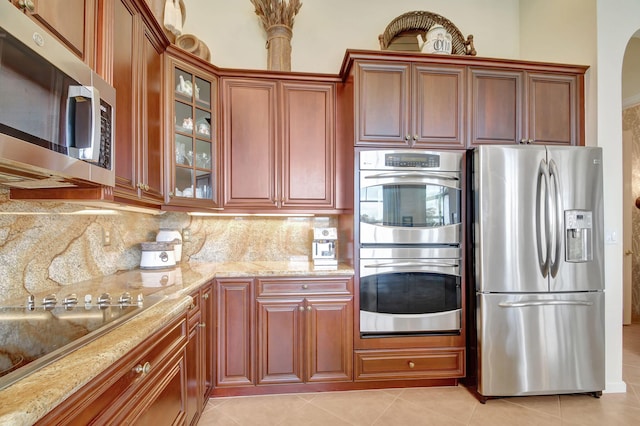 kitchen with decorative backsplash, light tile patterned flooring, light stone countertops, and appliances with stainless steel finishes