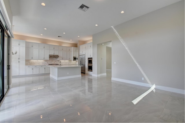 kitchen featuring sink, built in appliances, a center island with sink, decorative backsplash, and white cabinets