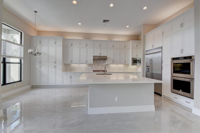 kitchen featuring sink, white cabinetry, tasteful backsplash, built in appliances, and an island with sink