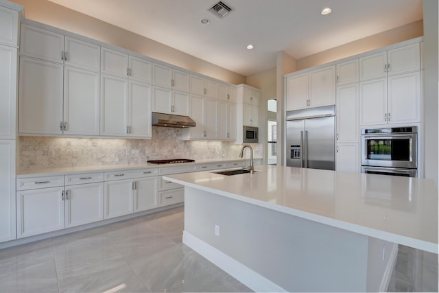 kitchen featuring built in appliances, sink, white cabinetry, and a center island with sink