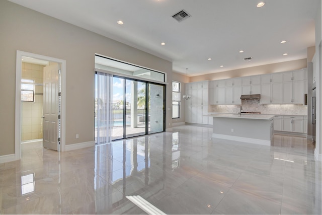 kitchen with white cabinetry, sink, an island with sink, and decorative backsplash