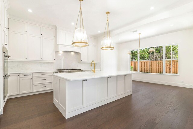 kitchen featuring dark hardwood / wood-style flooring, pendant lighting, white cabinets, a center island with sink, and backsplash