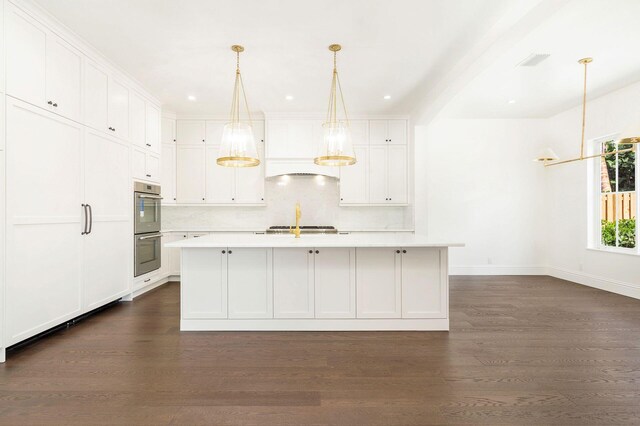 kitchen featuring white cabinets, dark wood-type flooring, appliances with stainless steel finishes, decorative backsplash, and a center island with sink