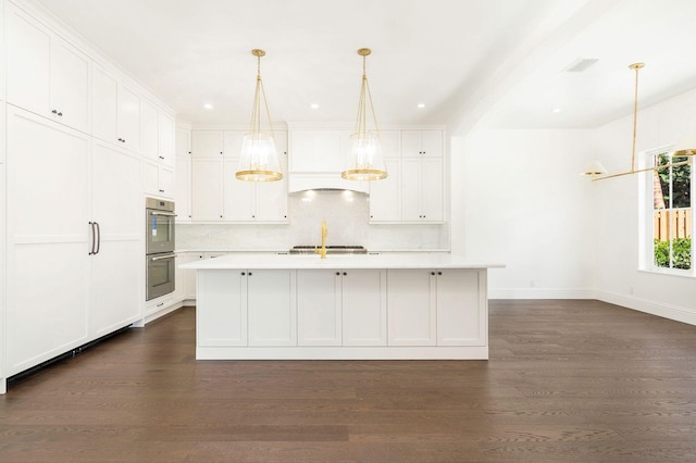 kitchen with white cabinetry, double oven, and a center island with sink