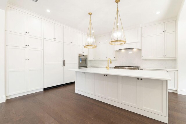 kitchen with tasteful backsplash, stainless steel oven, dark hardwood / wood-style flooring, decorative light fixtures, and a center island with sink