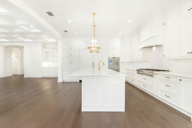 kitchen with appliances with stainless steel finishes, white cabinetry, an island with sink, hanging light fixtures, and dark wood-type flooring