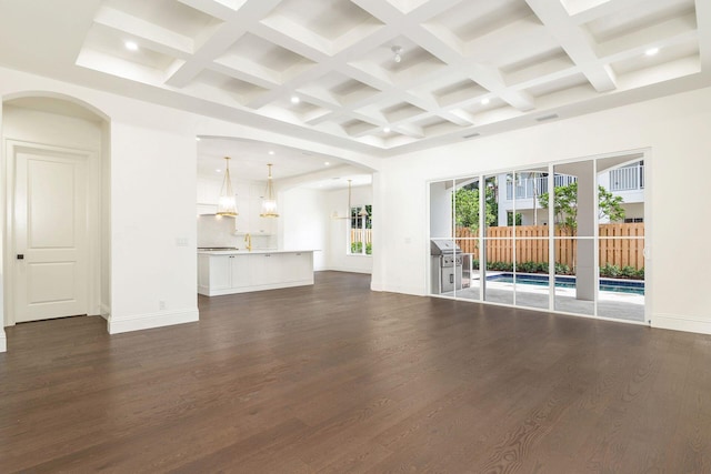 unfurnished living room featuring coffered ceiling, dark hardwood / wood-style floors, beamed ceiling, and a high ceiling