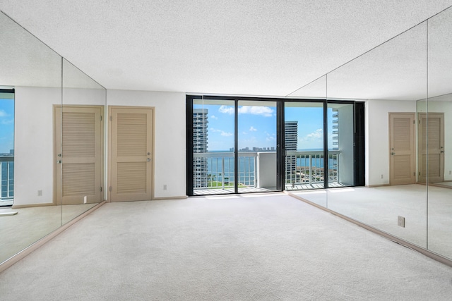 unfurnished bedroom featuring a water view, carpet floors, a textured ceiling, access to exterior, and floor to ceiling windows