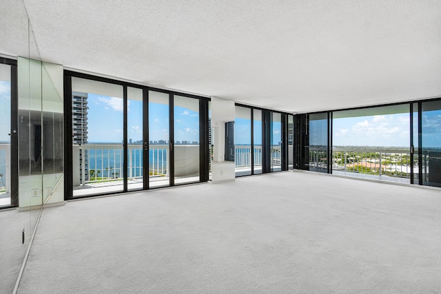 carpeted empty room featuring a water view, expansive windows, and a textured ceiling