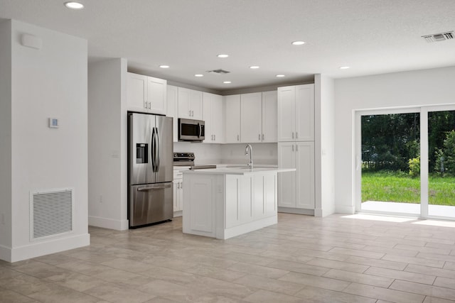 kitchen featuring a kitchen island with sink, sink, stainless steel appliances, and white cabinets