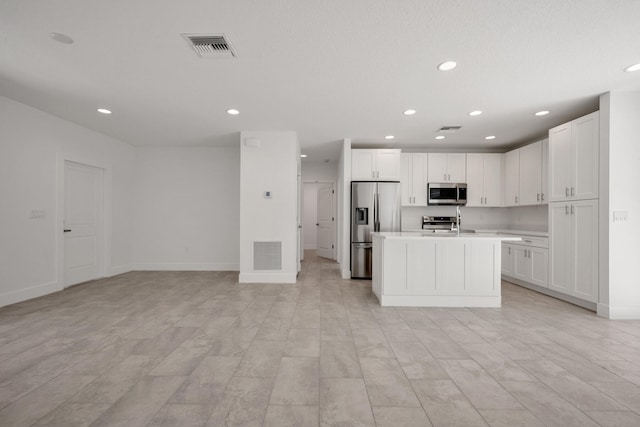 kitchen with a kitchen island with sink, light tile patterned floors, white cabinetry, and stainless steel appliances