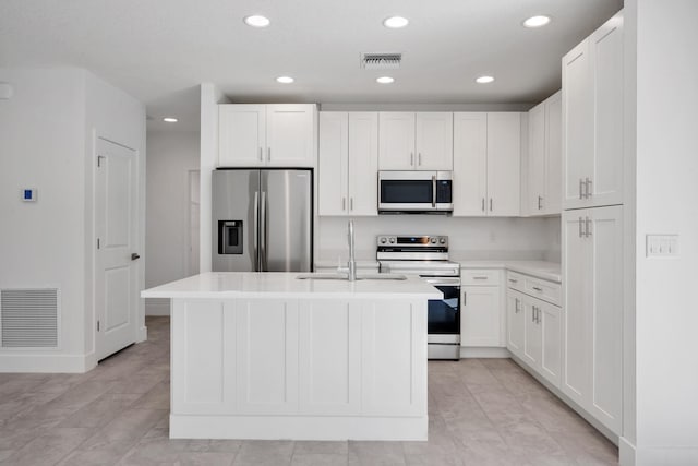 kitchen with light tile patterned flooring, sink, a kitchen island with sink, stainless steel appliances, and white cabinets