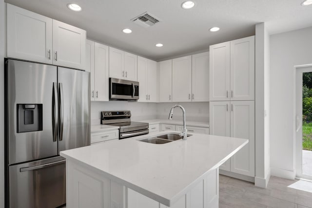 kitchen with a kitchen island with sink, white cabinets, appliances with stainless steel finishes, sink, and light tile patterned flooring