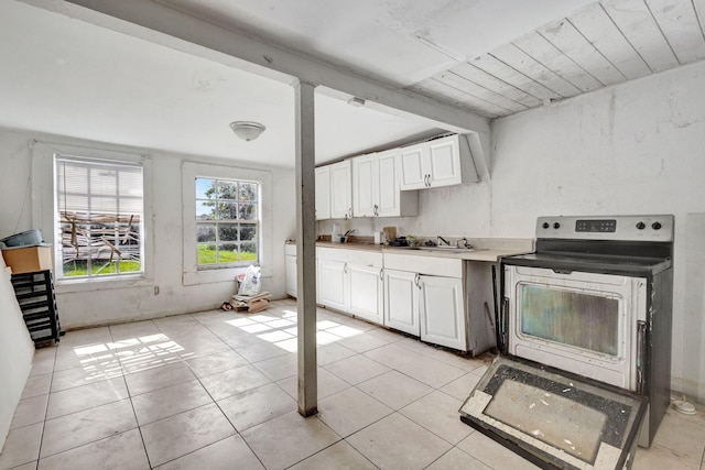 kitchen featuring electric range oven, light tile patterned floors, a sink, and white cabinets