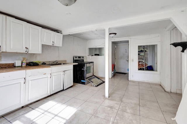 kitchen featuring electric range, light tile patterned flooring, a sink, and white cabinetry