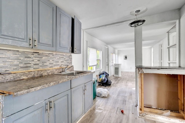 kitchen featuring tasteful backsplash, baseboards, gray cabinetry, light wood-type flooring, and a sink