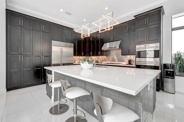 kitchen featuring appliances with stainless steel finishes, ornamental molding, a center island with sink, and light tile patterned floors