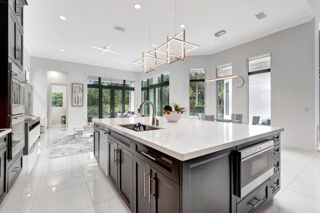 kitchen featuring light tile patterned flooring, pendant lighting, crown molding, sink, and a kitchen island with sink