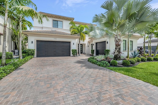 view of front of property featuring central air condition unit, a garage, a tiled roof, decorative driveway, and stucco siding