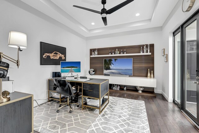 home office featuring ceiling fan, hardwood / wood-style floors, and a tray ceiling