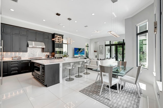 kitchen with backsplash, gas cooktop, pendant lighting, a center island with sink, and ornamental molding