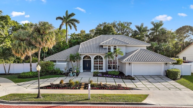 mediterranean / spanish home featuring an attached garage, concrete driveway, a tile roof, and fence