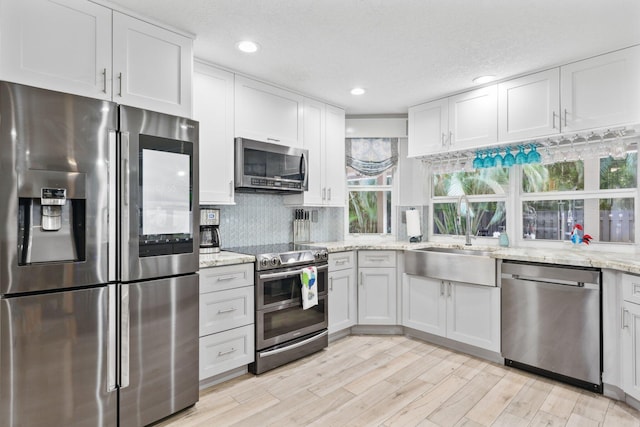 kitchen with white cabinets, light stone counters, stainless steel appliances, light wood-style floors, and a sink