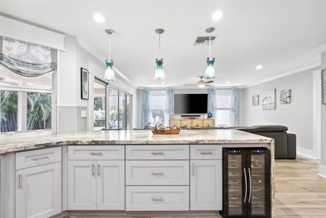 kitchen with wine cooler, light stone counters, open floor plan, tasteful backsplash, and crown molding