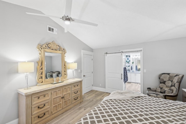 bedroom with lofted ceiling, visible vents, light wood-style flooring, a barn door, and baseboards