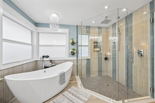 full bath featuring tile walls, a soaking tub, a notable chandelier, and a shower stall