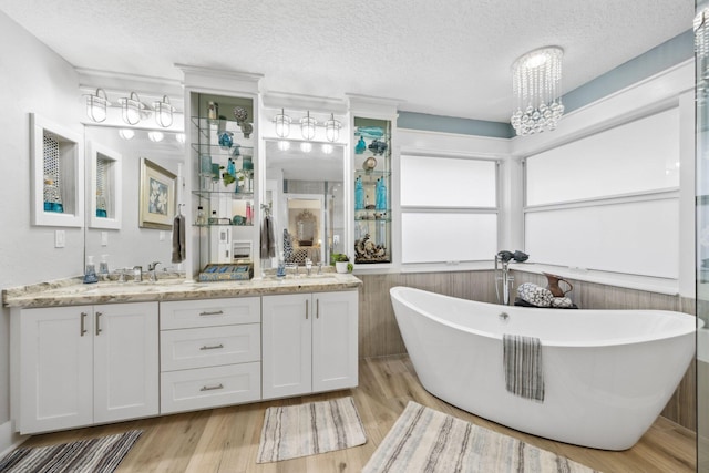 full bathroom featuring double vanity, a freestanding tub, a textured ceiling, and wood finished floors