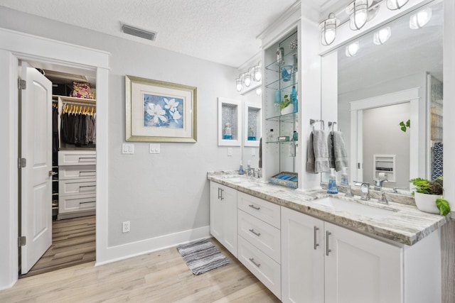 bathroom with double vanity, visible vents, wood finished floors, a walk in closet, and a sink