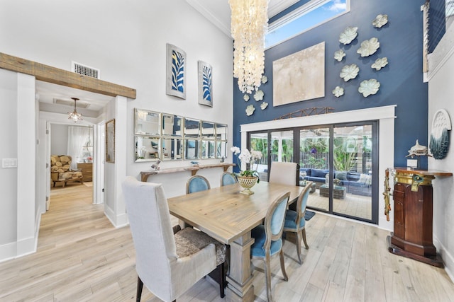 dining space featuring a chandelier, visible vents, light wood-style flooring, and a towering ceiling