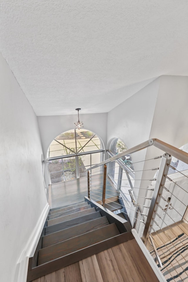 stairs with a chandelier, a textured ceiling, and wood finished floors