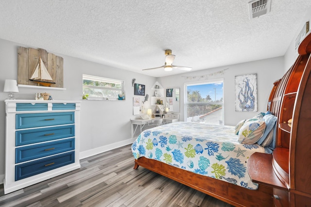 bedroom featuring baseboards, multiple windows, visible vents, and wood finished floors