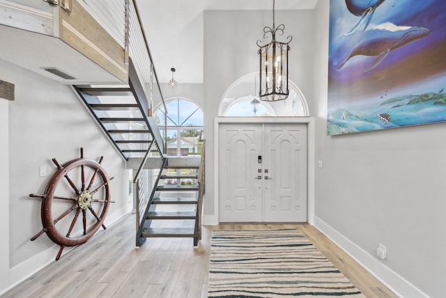 foyer with a notable chandelier, wood finished floors, visible vents, baseboards, and stairs