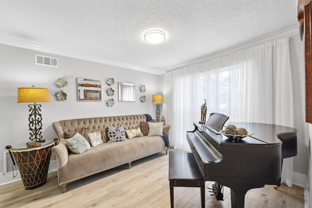 living room with light wood-style flooring, a textured ceiling, visible vents, and crown molding